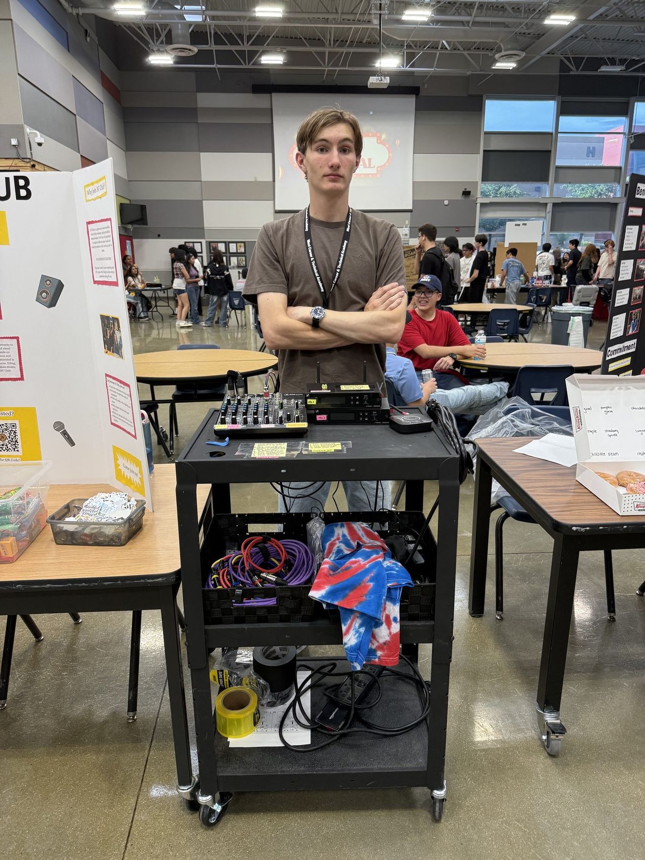 An AV Club member standing behind a cart holding a sound mixer and cables